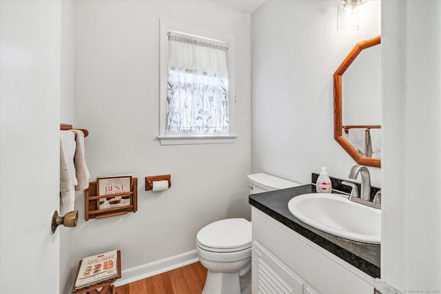 half bath with vanity, toilet, wood finished floors, and baseboards