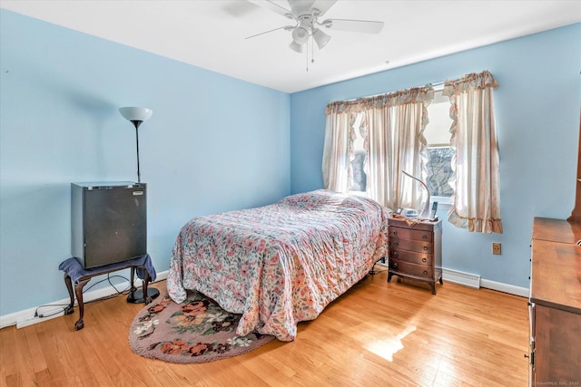 bedroom with a baseboard heating unit, baseboards, wood finished floors, and a ceiling fan