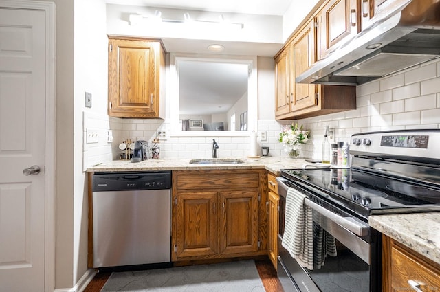 kitchen featuring light stone counters, a sink, decorative backsplash, stainless steel appliances, and under cabinet range hood