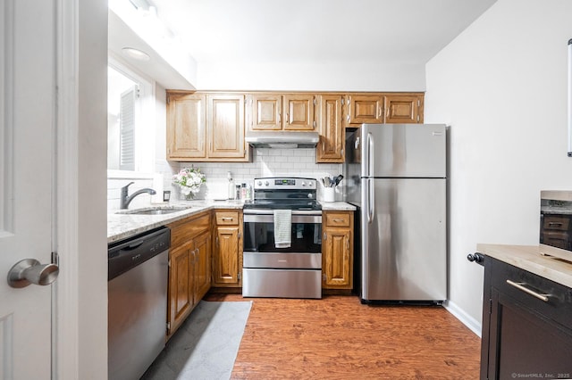 kitchen featuring a sink, decorative backsplash, stainless steel appliances, under cabinet range hood, and light wood-type flooring