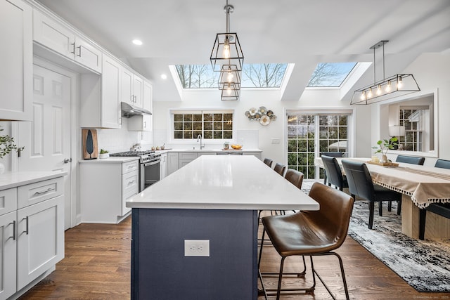 kitchen featuring dark wood-type flooring, under cabinet range hood, lofted ceiling with skylight, a breakfast bar area, and stainless steel gas range