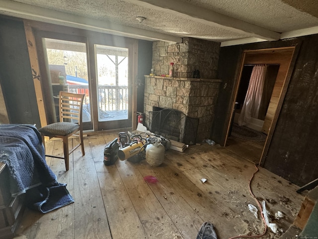 living area with beam ceiling, a textured ceiling, a fireplace, and hardwood / wood-style flooring