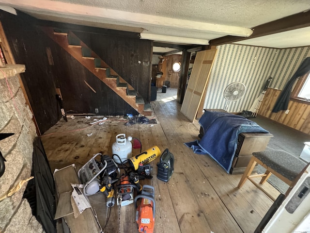 unfurnished living room featuring beamed ceiling, wood walls, stairs, hardwood / wood-style floors, and a textured ceiling