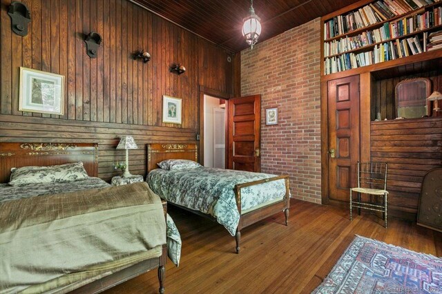 bedroom with wooden walls, wooden ceiling, brick wall, and wood finished floors