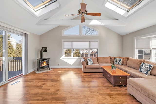 living area featuring visible vents, baseboards, light wood-type flooring, vaulted ceiling with skylight, and a ceiling fan