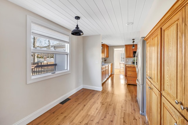 kitchen featuring baseboards, visible vents, freestanding refrigerator, light wood-style floors, and decorative light fixtures