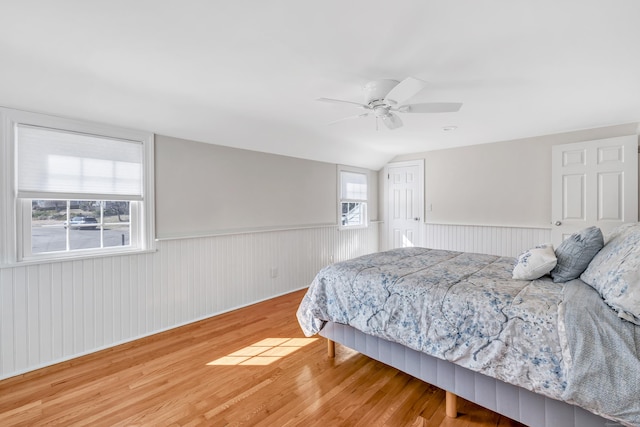 bedroom with vaulted ceiling, wood finished floors, a wainscoted wall, and ceiling fan