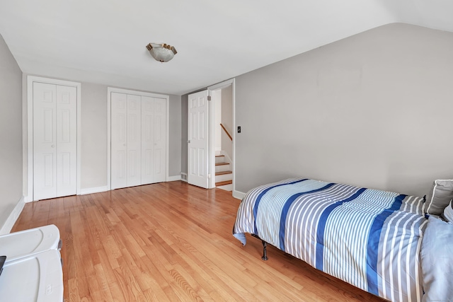 bedroom featuring two closets, baseboards, and light wood-style floors