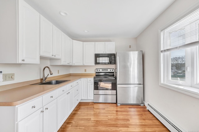 kitchen featuring light wood-type flooring, a sink, a baseboard heating unit, white cabinetry, and stainless steel appliances