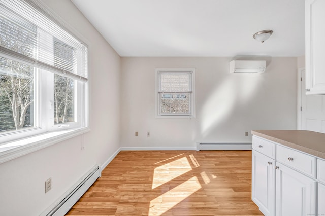 kitchen featuring light wood finished floors, white cabinetry, a wall unit AC, and a baseboard radiator