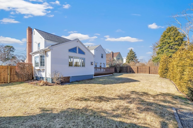 rear view of property with a yard, a wooden deck, a fenced backyard, and a chimney