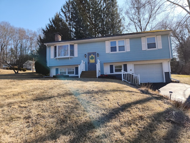 bi-level home featuring a front lawn, an attached garage, driveway, and a chimney