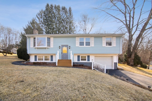 bi-level home with aphalt driveway, a front lawn, an attached garage, and a chimney