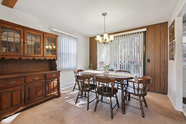 dining room featuring light carpet, a notable chandelier, a textured ceiling, wooden walls, and baseboards