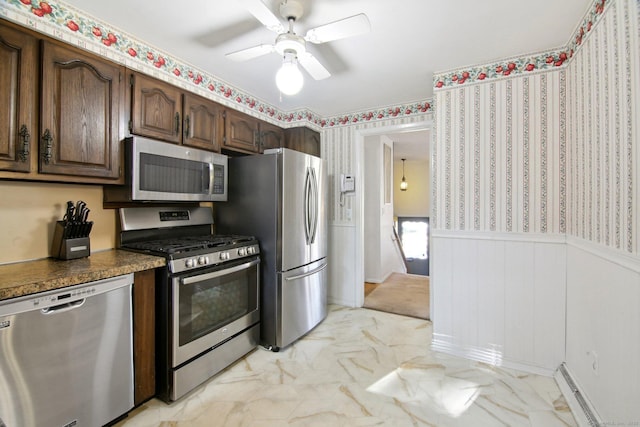 kitchen with a wainscoted wall, appliances with stainless steel finishes, marble finish floor, a ceiling fan, and a baseboard radiator