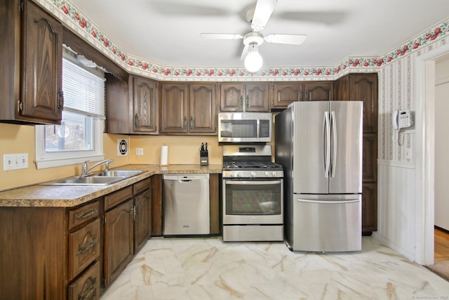 kitchen with wainscoting, marble finish floor, stainless steel appliances, a ceiling fan, and a sink