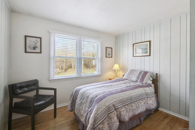 bedroom featuring baseboards, wood finished floors, and wood walls