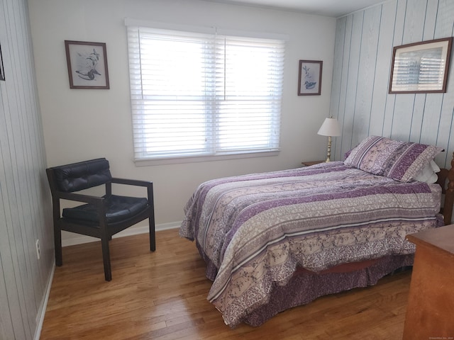 bedroom with wood finished floors, baseboards, and wood walls