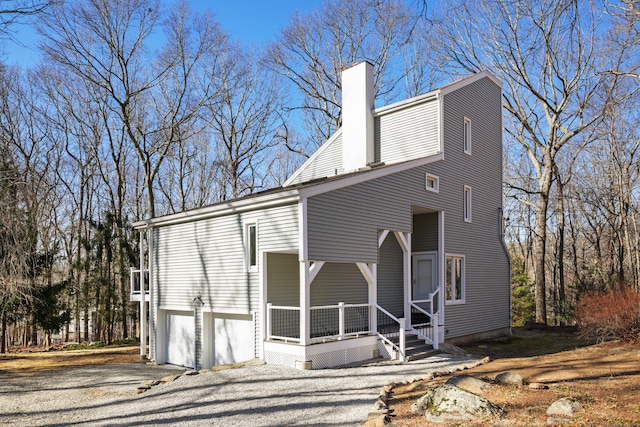 view of front of home with covered porch, an attached garage, a chimney, and driveway