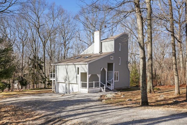 view of front of house with a shingled roof, a garage, driveway, and a chimney