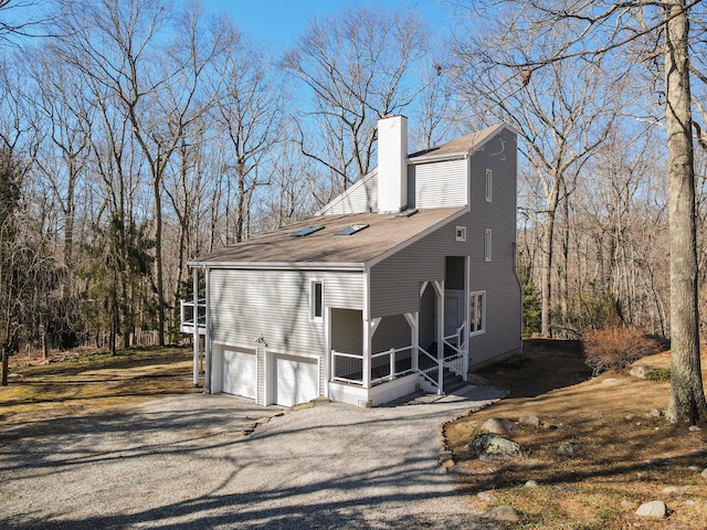 view of front of house with a shingled roof, aphalt driveway, a garage, and a chimney