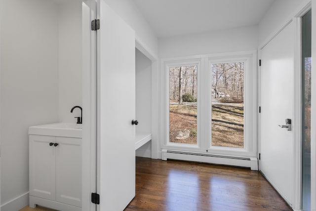 hallway featuring dark wood-style floors, baseboard heating, and a sink