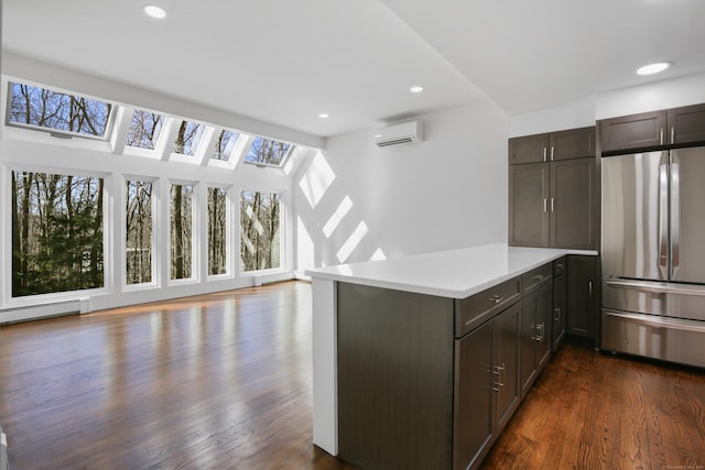 kitchen with light countertops, a wall unit AC, a peninsula, freestanding refrigerator, and dark wood-style floors