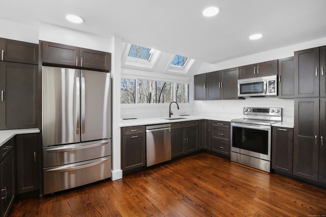 kitchen featuring vaulted ceiling with skylight, a sink, light countertops, dark wood-type flooring, and appliances with stainless steel finishes