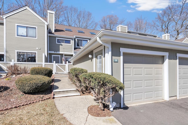 exterior space with driveway, a gate, fence, a garage, and a chimney