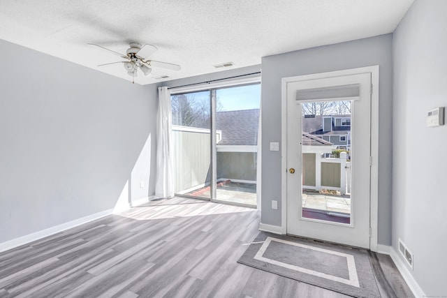 unfurnished room featuring visible vents, a textured ceiling, baseboards, and wood finished floors