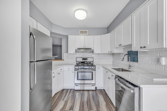 kitchen with dark wood finished floors, a sink, light countertops, under cabinet range hood, and appliances with stainless steel finishes