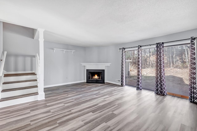 unfurnished living room featuring a fireplace with flush hearth, a textured ceiling, wood finished floors, baseboards, and stairs