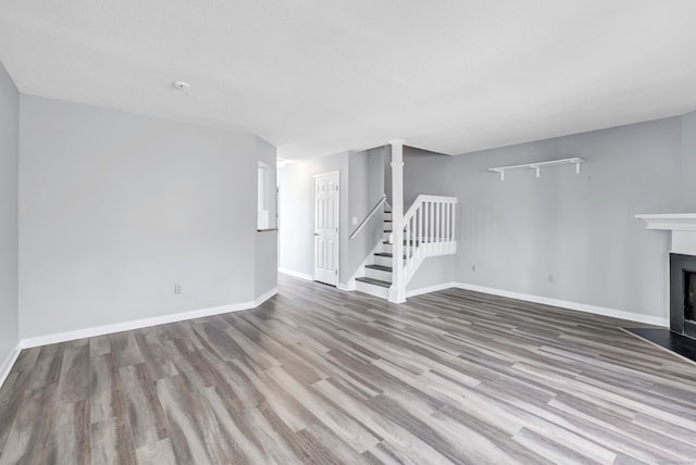 unfurnished living room featuring stairway, a fireplace with flush hearth, wood finished floors, and baseboards