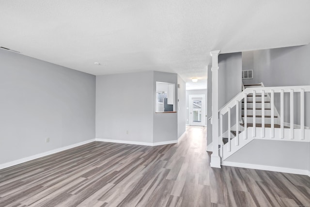 unfurnished room with stairway, wood finished floors, visible vents, and baseboards