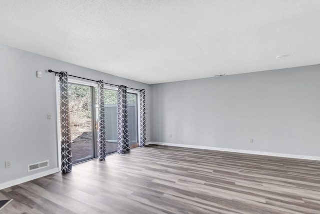 empty room featuring wood finished floors, visible vents, and baseboards