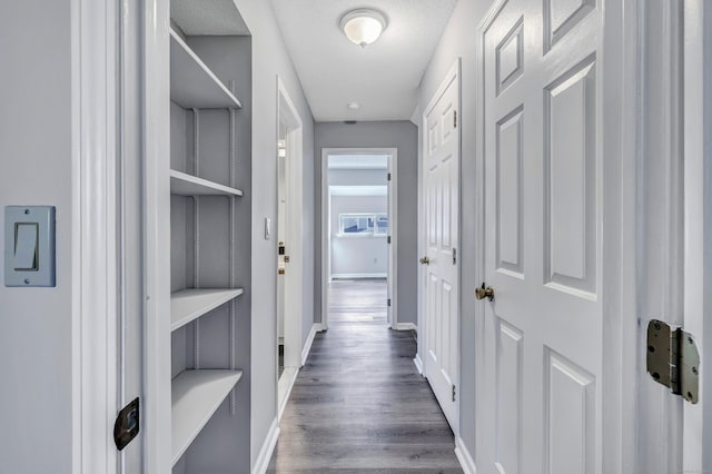 corridor featuring built in shelves, dark wood-type flooring, and baseboards