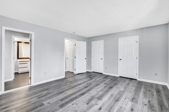 unfurnished bedroom with ensuite bath, wood finished floors, and baseboards