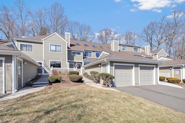 exterior space with a front yard, roof with shingles, an attached garage, a chimney, and aphalt driveway