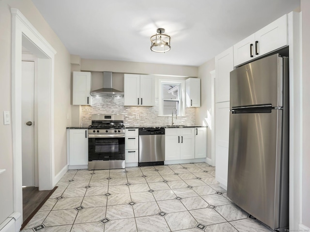 kitchen with a sink, baseboard heating, appliances with stainless steel finishes, wall chimney exhaust hood, and backsplash