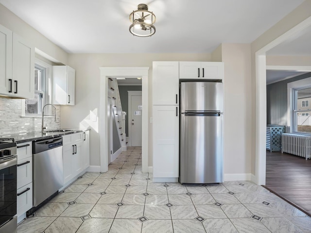 kitchen with backsplash, radiator, stainless steel appliances, white cabinetry, and a sink