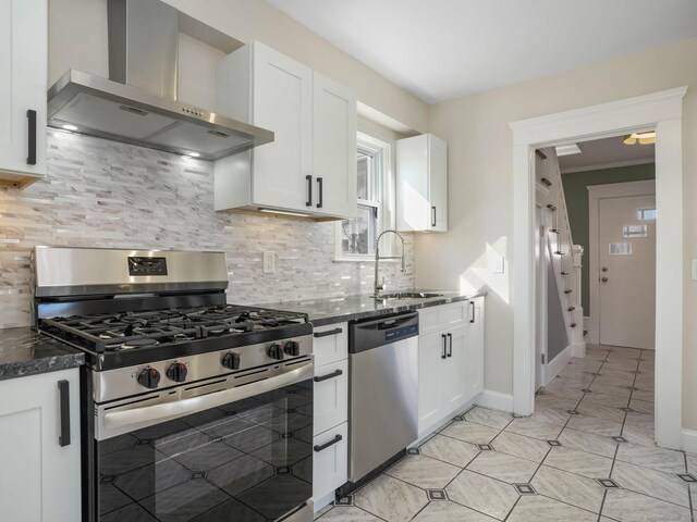 kitchen featuring a sink, stainless steel appliances, white cabinets, wall chimney exhaust hood, and backsplash