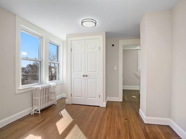 interior space with a closet, baseboards, radiator, and wood finished floors