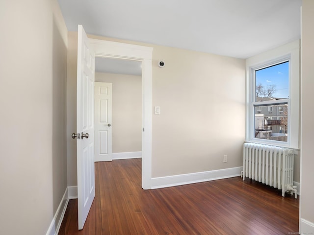 empty room featuring dark wood finished floors, radiator, and baseboards