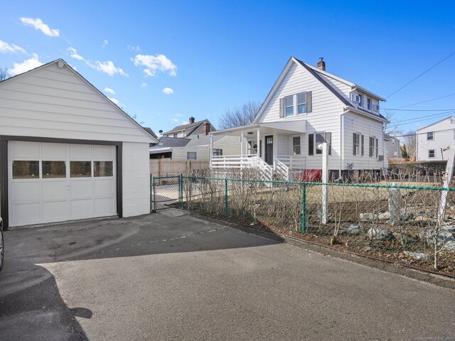 view of front facade featuring covered porch, a chimney, an outdoor structure, a fenced front yard, and a detached garage