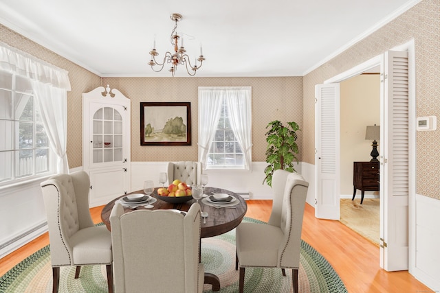 dining room with a wainscoted wall, wallpapered walls, light wood-type flooring, and an inviting chandelier