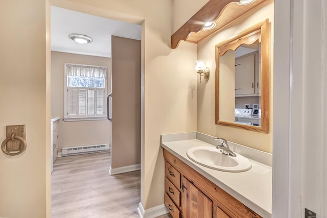 bathroom featuring a baseboard heating unit, baseboards, wood finished floors, washer and dryer, and vanity