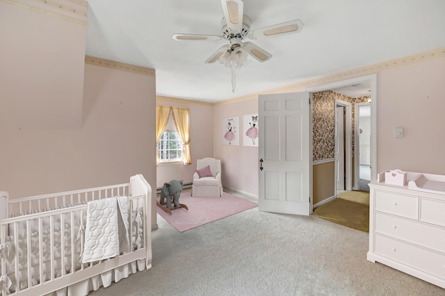 carpeted bedroom featuring a nursery area, a ceiling fan, baseboards, and ornamental molding