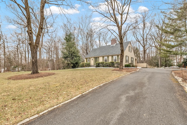 view of front of home featuring driveway, a front lawn, a chimney, and a shingled roof