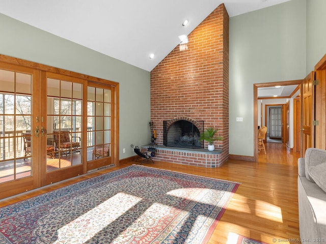 living area featuring a fireplace, high vaulted ceiling, baseboards, and wood finished floors