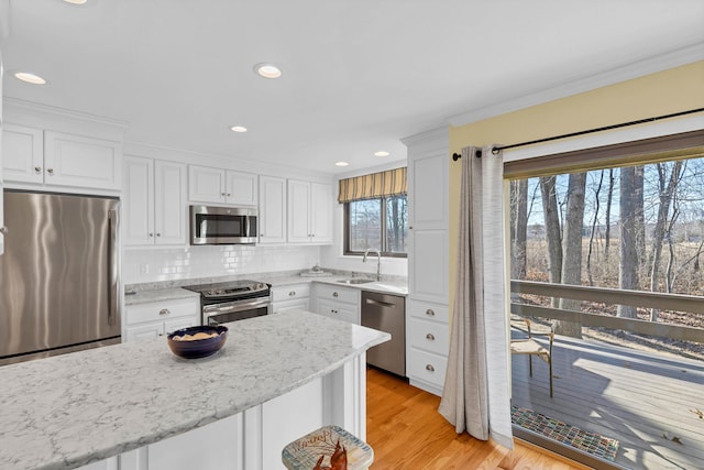 kitchen featuring a sink, appliances with stainless steel finishes, white cabinets, light wood finished floors, and light stone countertops